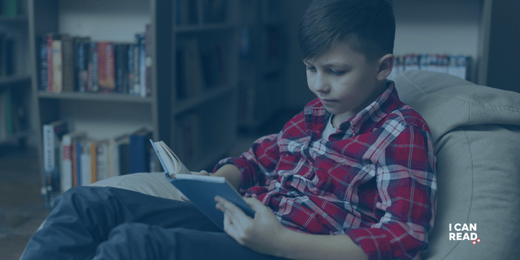 A teenage boy in a red check shirt is reading on a comfy sofa.