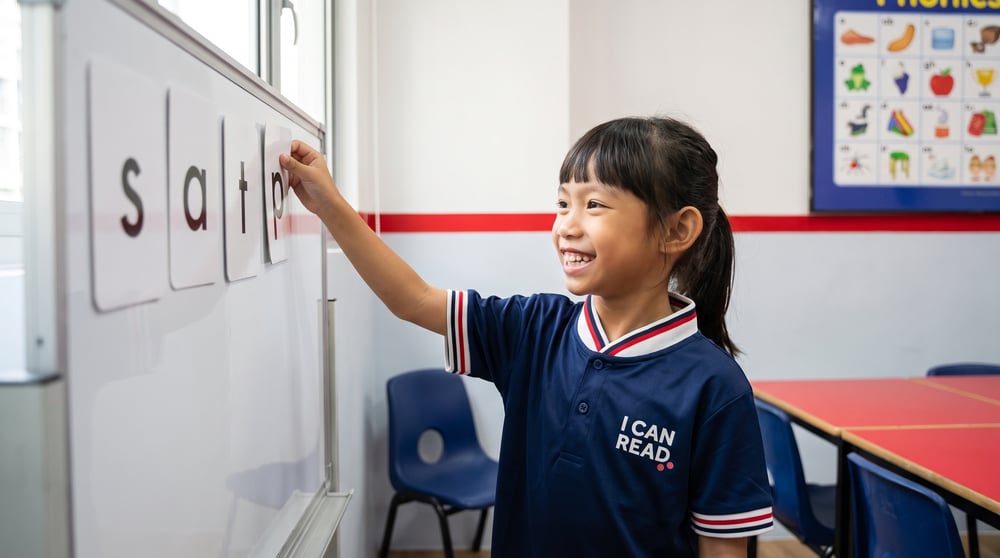 Young girl placing the letter card p beside s, a and t on a classroom whiteboard