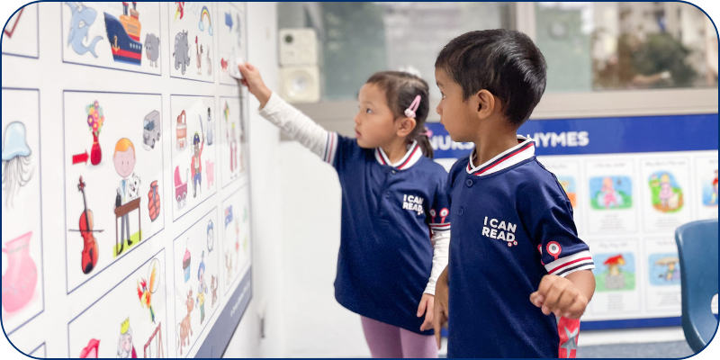 Two students in an I Can Read class pointing to a picture board Two students in an I Can Read class pointing to a picture board